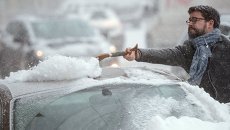 Автовладелец счищает снег с автомобиля в Москве Автовладелец счищает снег с автомобиля в Москве