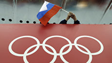 Болельщик держит российский флаг над логотипом олимпийских игр. Архивное фото Болельщик держит российский флаг над логотипом олимпийских игр. Архивное фото