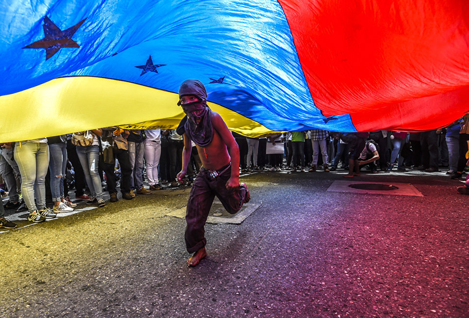 Мальчик пробегает под флагом Венесуэлы во время протестов в Каракасе