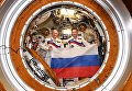 Российские космонавты Олег Артемьев и Сергей Прокопьев с флагом страны в День Государственного флага на борту МКС Российские космонавты Олег Артемьев и Сергей Прокопьев с флагом страны в День Государственного флага на борту МКС